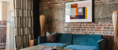 A modern living room with a blue sofa, a coffee table, and a large abstract painting on a brick wall.