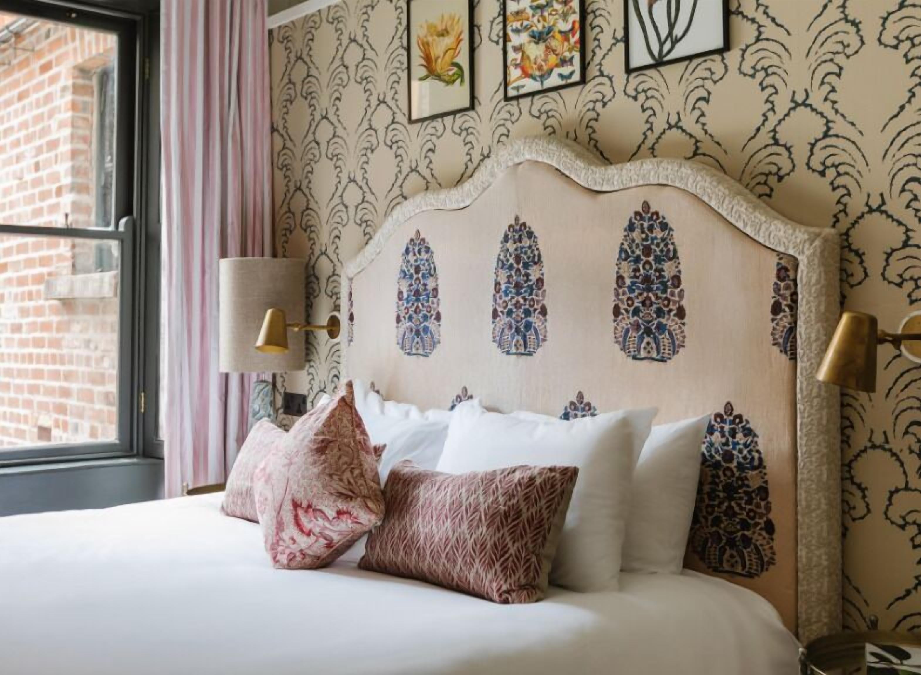A neatly made bed with patterned pillows, a decorative headboard, and wall-mounted lamps.