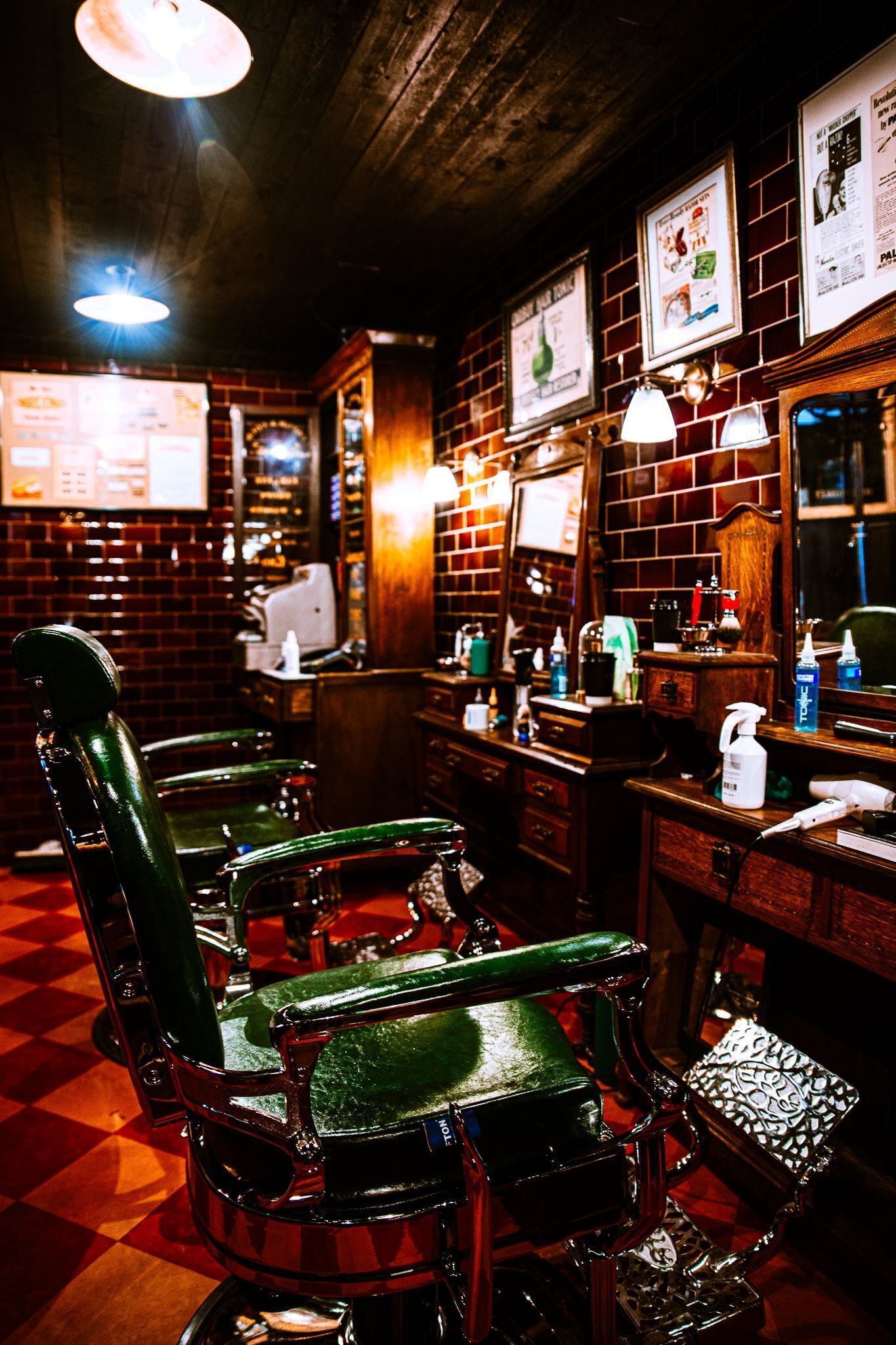 Una barbería con sillas de barbero verdes antiguas, una pared de ladrillo y carteles enmarcados.