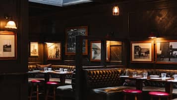A dimly lit restaurant with wooden walls, framed pictures, and a high ceiling with a skylight.