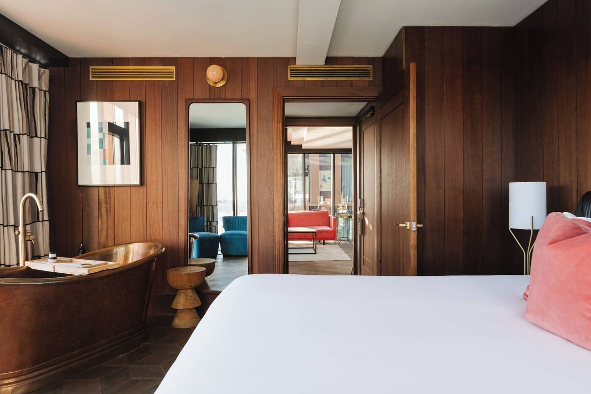 Habitación de hotel moderna con una cama grande, una bañera de madera, un sofá rojo y vistas a la ciudad.
