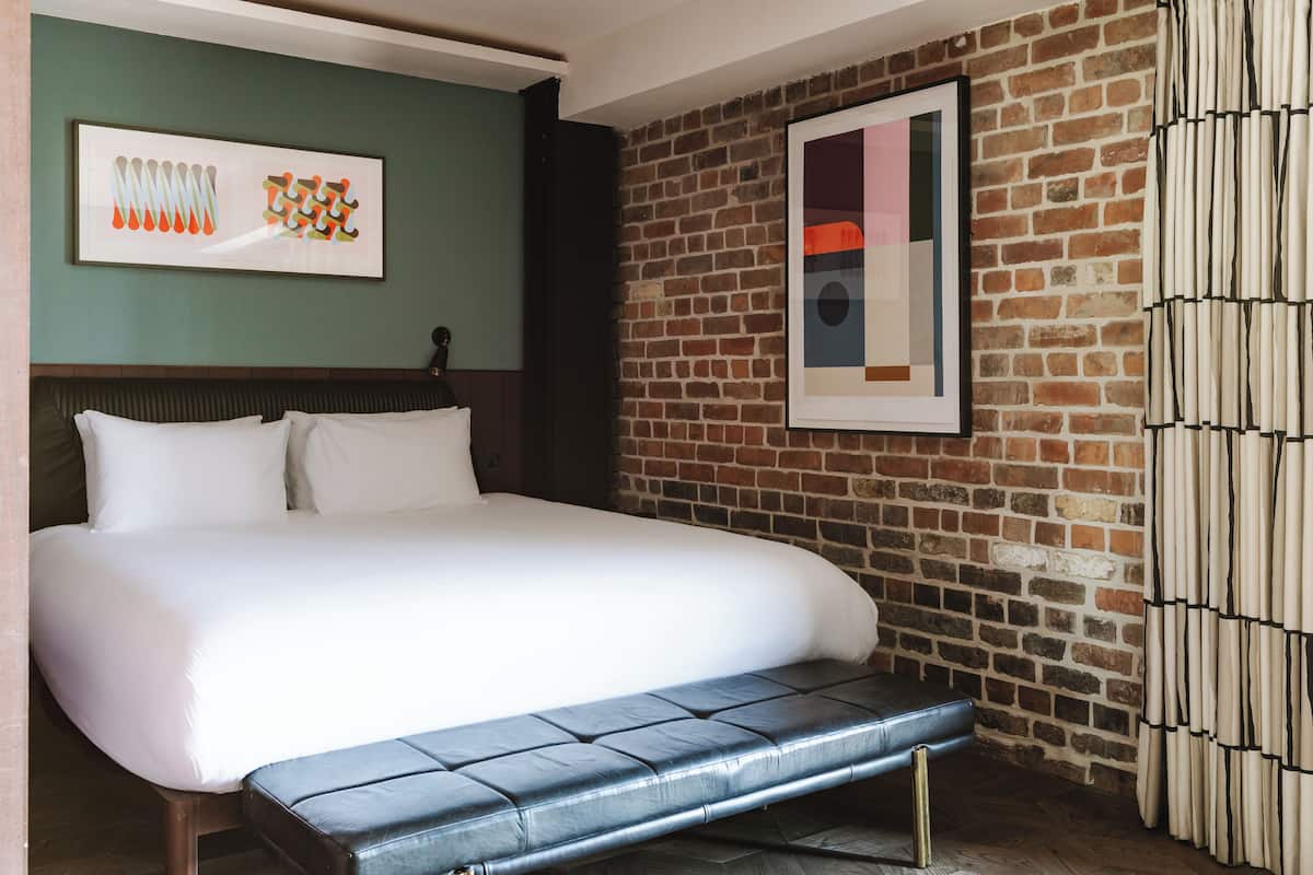 Una habitación de hotel con una cama grande, un banco, una pared de ladrillo y dos obras de arte enmarcadas.