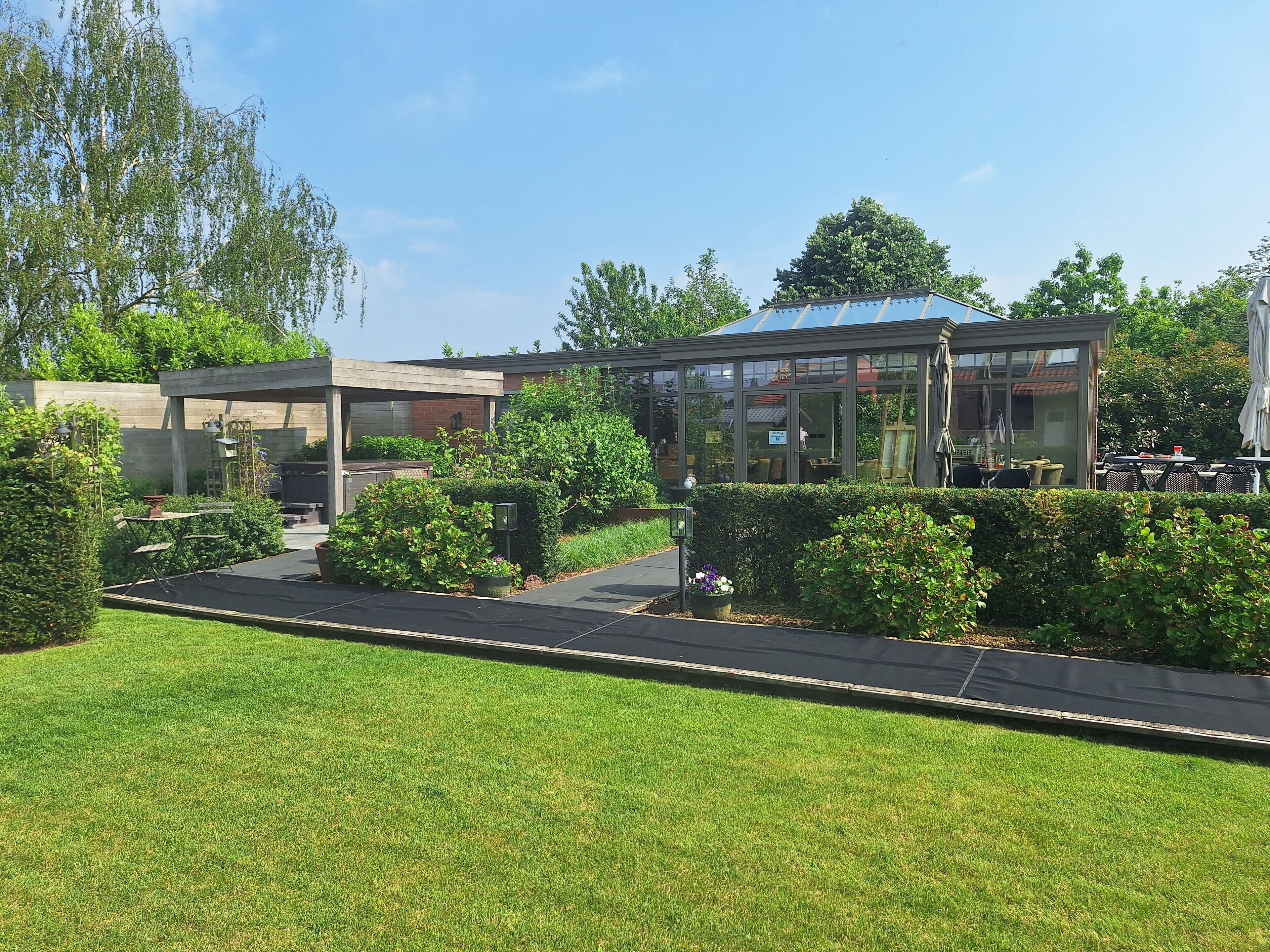 Een modern buiten zitgedeelte met een glazen omheining, omgeven door verzorgde hagen en een gazon.