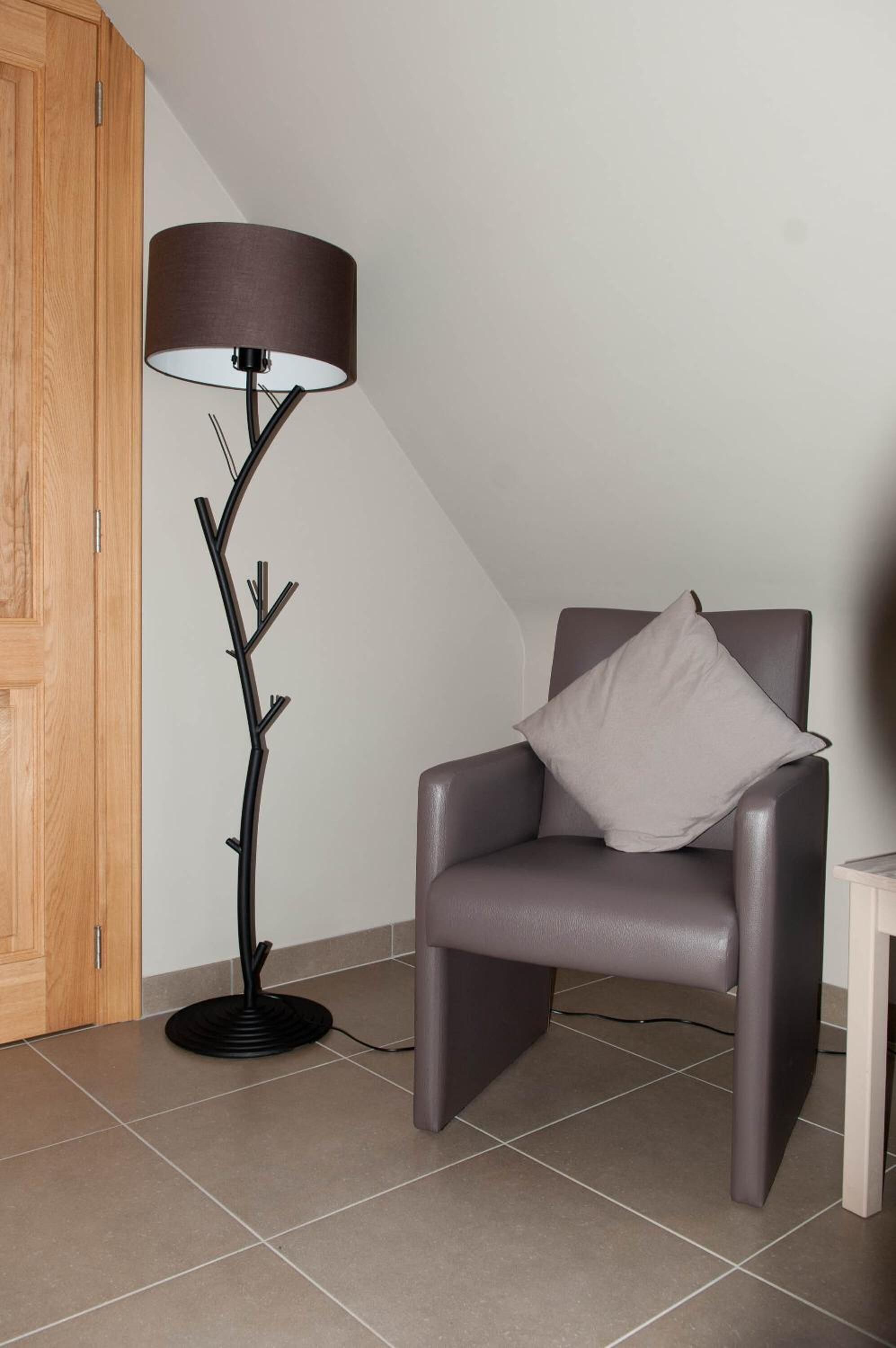 Ett modernt rum med en mörk läderfåtölj, en golvlampa med en grenliknande design och en trädörr.