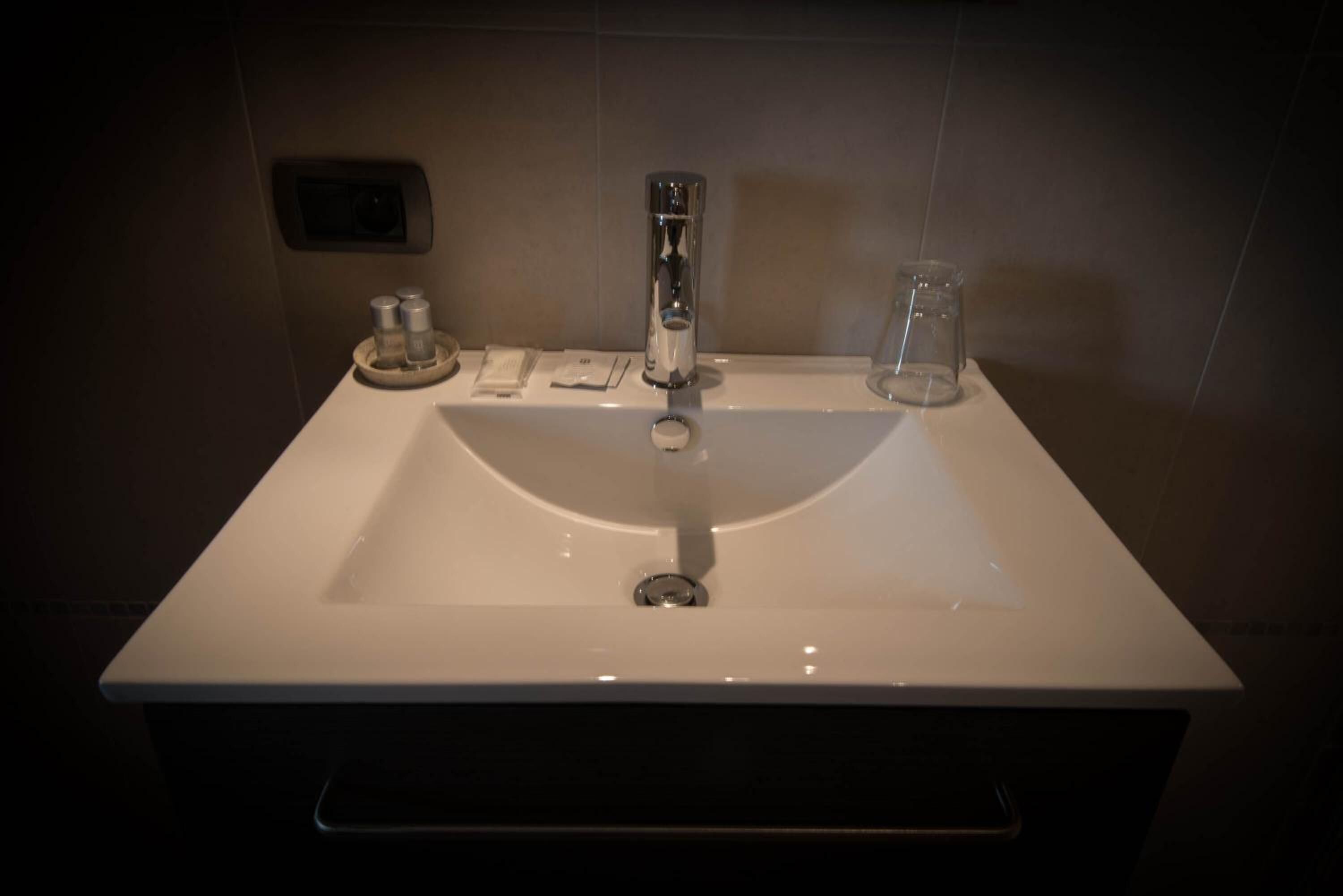 A bathroom sink with a chrome faucet, a soap dispenser, and a glass container.