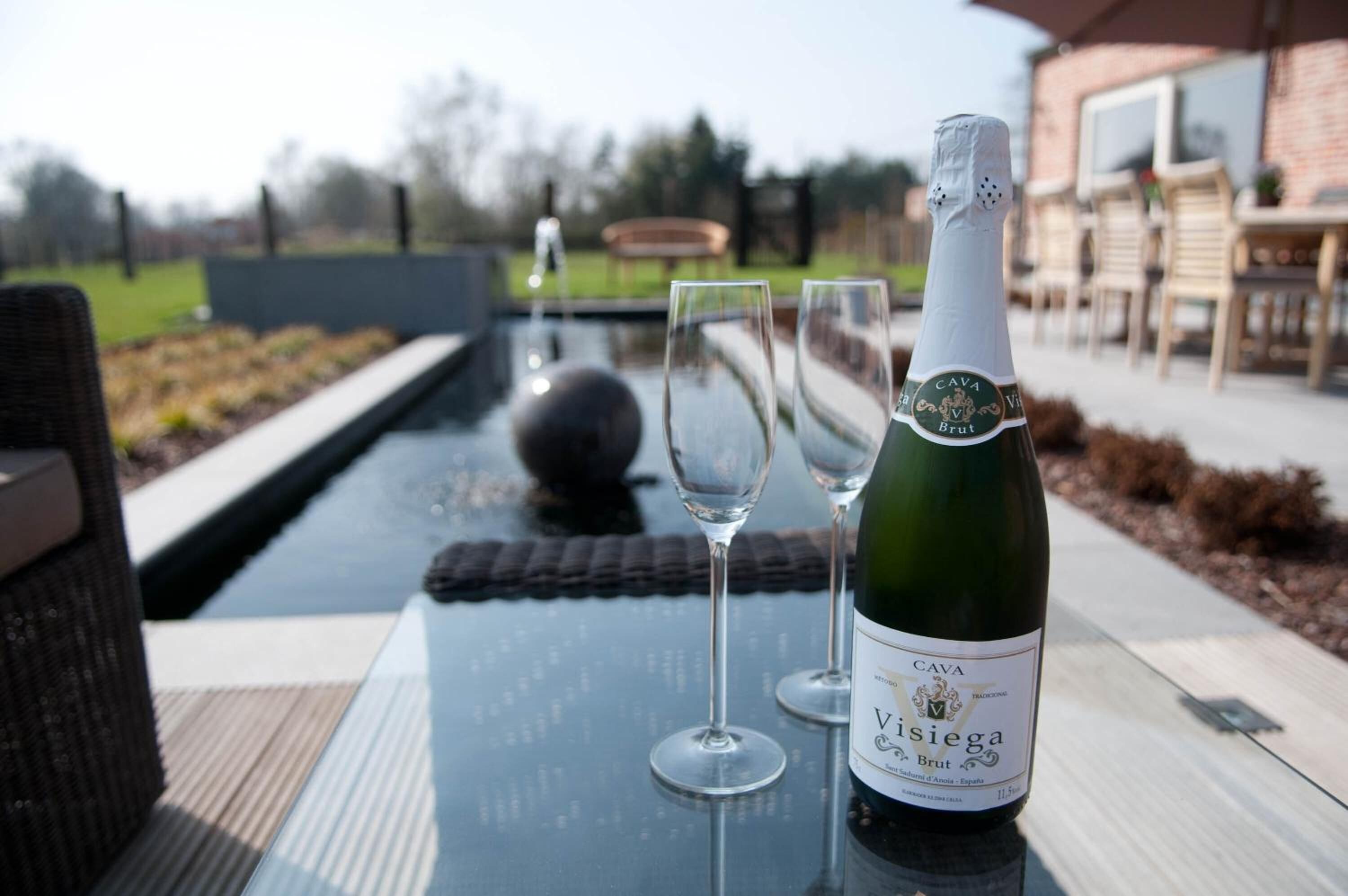 A bottle of Cava Visiega Brut wine on a table with two empty wine glasses.