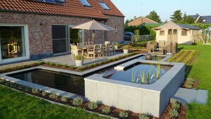 Une maison moderne dotée d’un patio, d’un espace salon extérieur, d’une piscine et de panneaux solaires sur le toit.