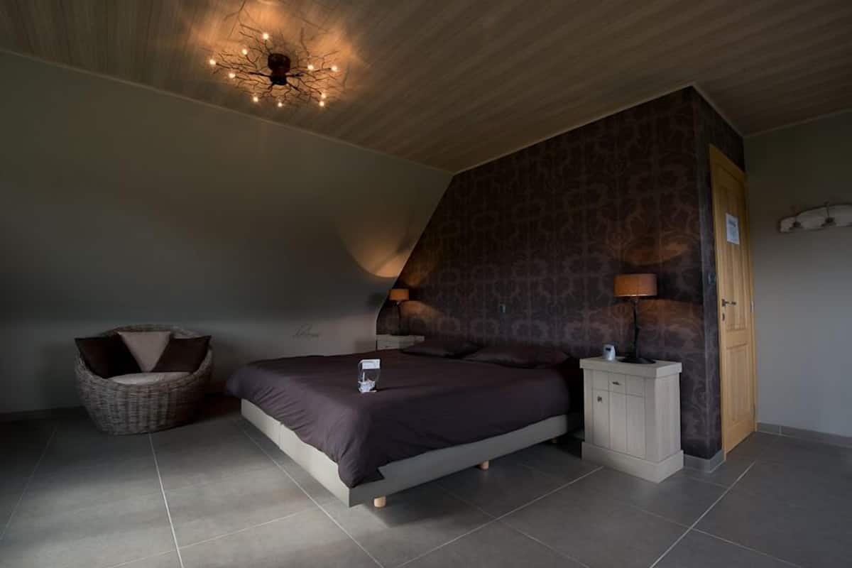 Un dormitorio con cama, mesita de noche, silla y pared con diseño.