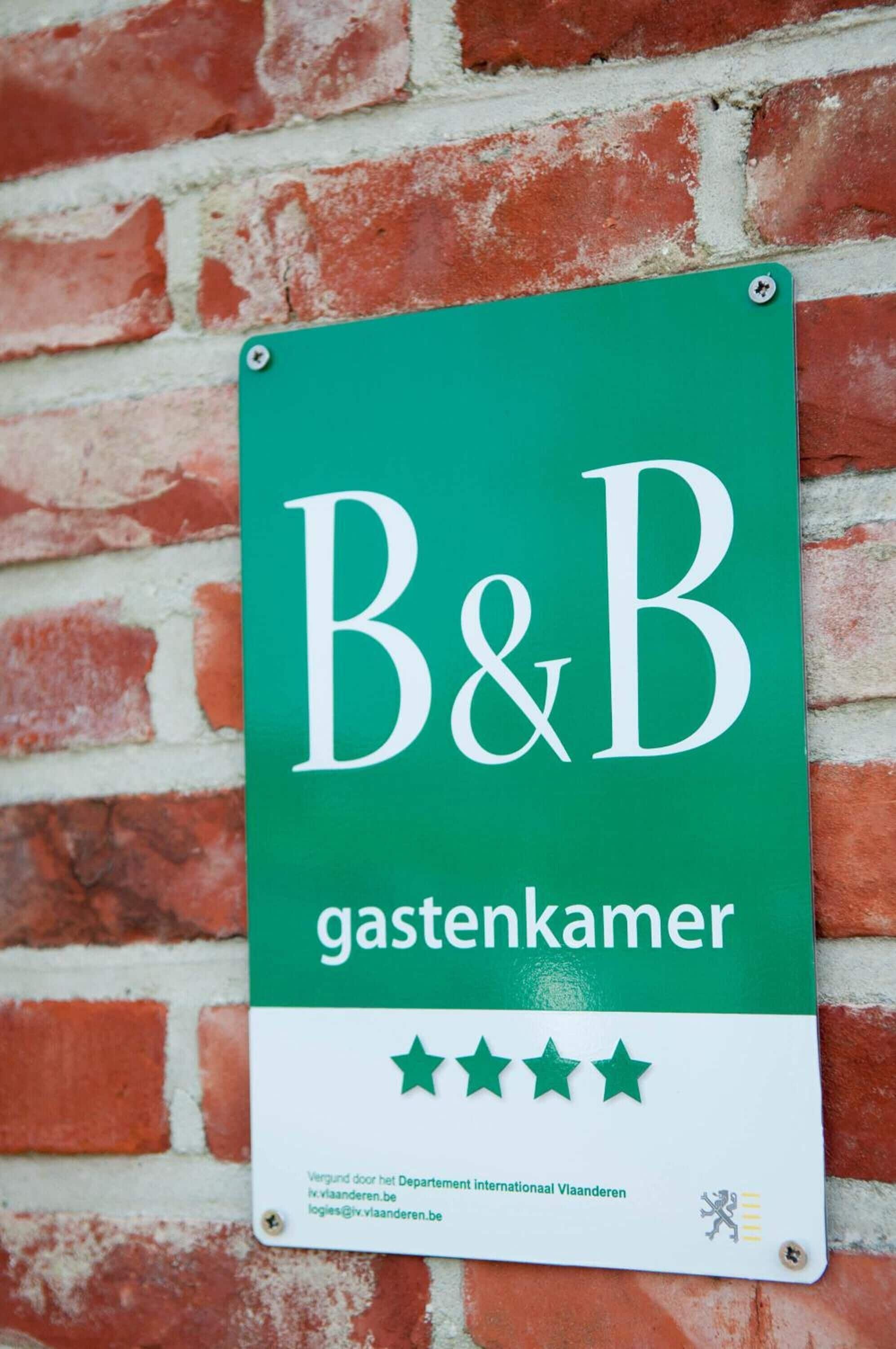 Un letrero verde con la inscripción 'B&B gastenkamer' y una calificación de cuatro estrellas, sujeto a una pared de ladrillo.
