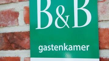 Un letrero verde con la inscripción 'B&B gastenkamer' y una calificación de cuatro estrellas, sujeto a una pared de ladrillo.
