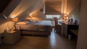 Une chambre mansardée agréable et bien éclairée, dotée d’un lit, d’un bureau et d’une chaise, et agrémentée d’un puits de lumière et d’une grande fenêtre.