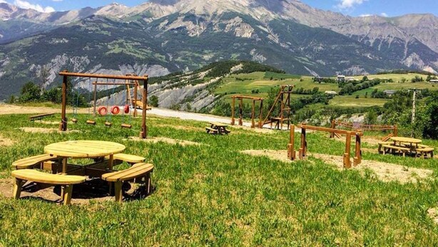Un espacio de picnic con bancos y mesas de madera, con montañas y cielo despejado de fondo.