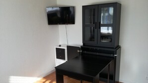 Una habitación con una mesa negra, un armario blanco y un armario negro con puertas de cristal.