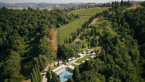 Vue aérienne d’un complexe hôtelier doté d’une piscine, entouré d’une forêt dense et de collines ondulantes.
