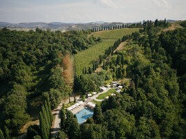 Vista aérea de um resort com piscina, rodeado por uma floresta densa e colinas ondulantes.