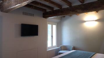 Ein Schlafzimmer mit einem Bett, einem Fernsehgerät an der Wand, einem Fenster und einem Sessel.