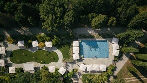 An aerial view of a pool area with a rectangular pool, surrounded by white umbrellas, and a landscaped area with a winding path. -  Relais Roncolo 1888 - Small Luxury Hotels of the World (Quattro Castella)