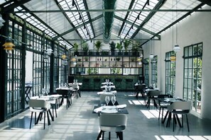 Un vaste espace de restauration intérieur, doté de hauts plafonds et de grandes fenêtres, où les tables et les chaises sont disposées avec soin.