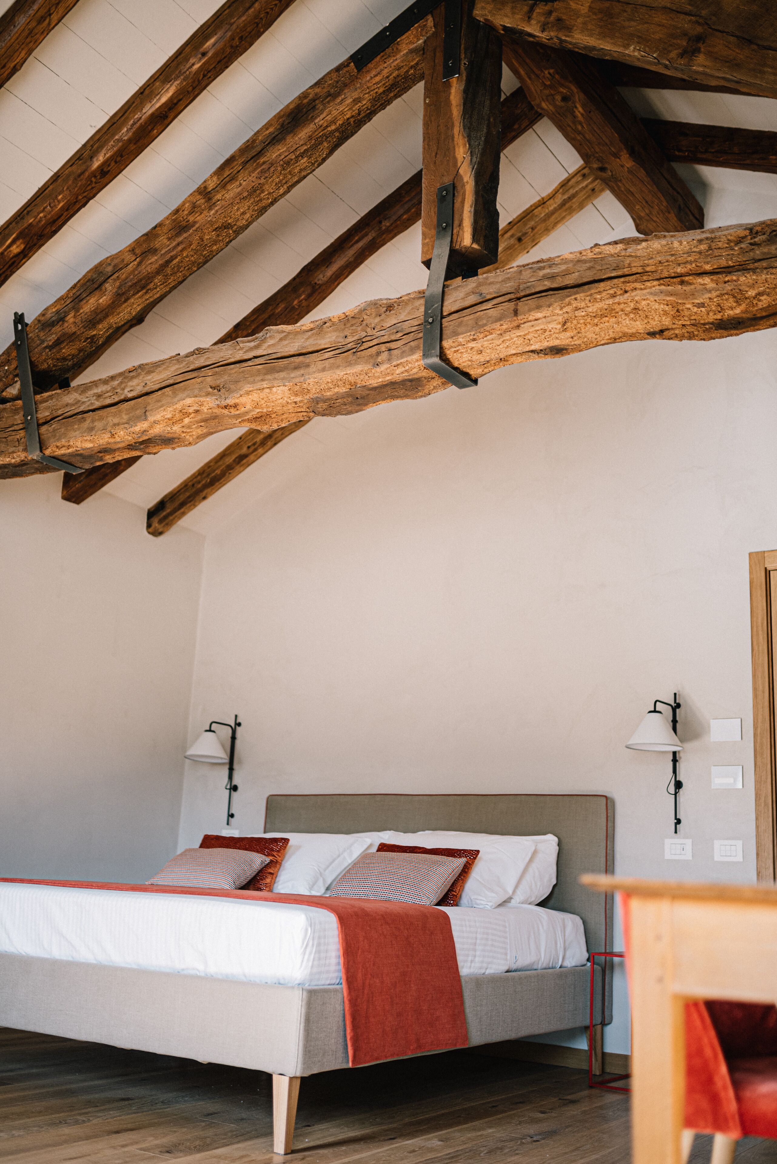 A bedroom with a wooden ceiling, a bed with white bedding and a red blanket, two bedside lamps, and a wooden nightstand.