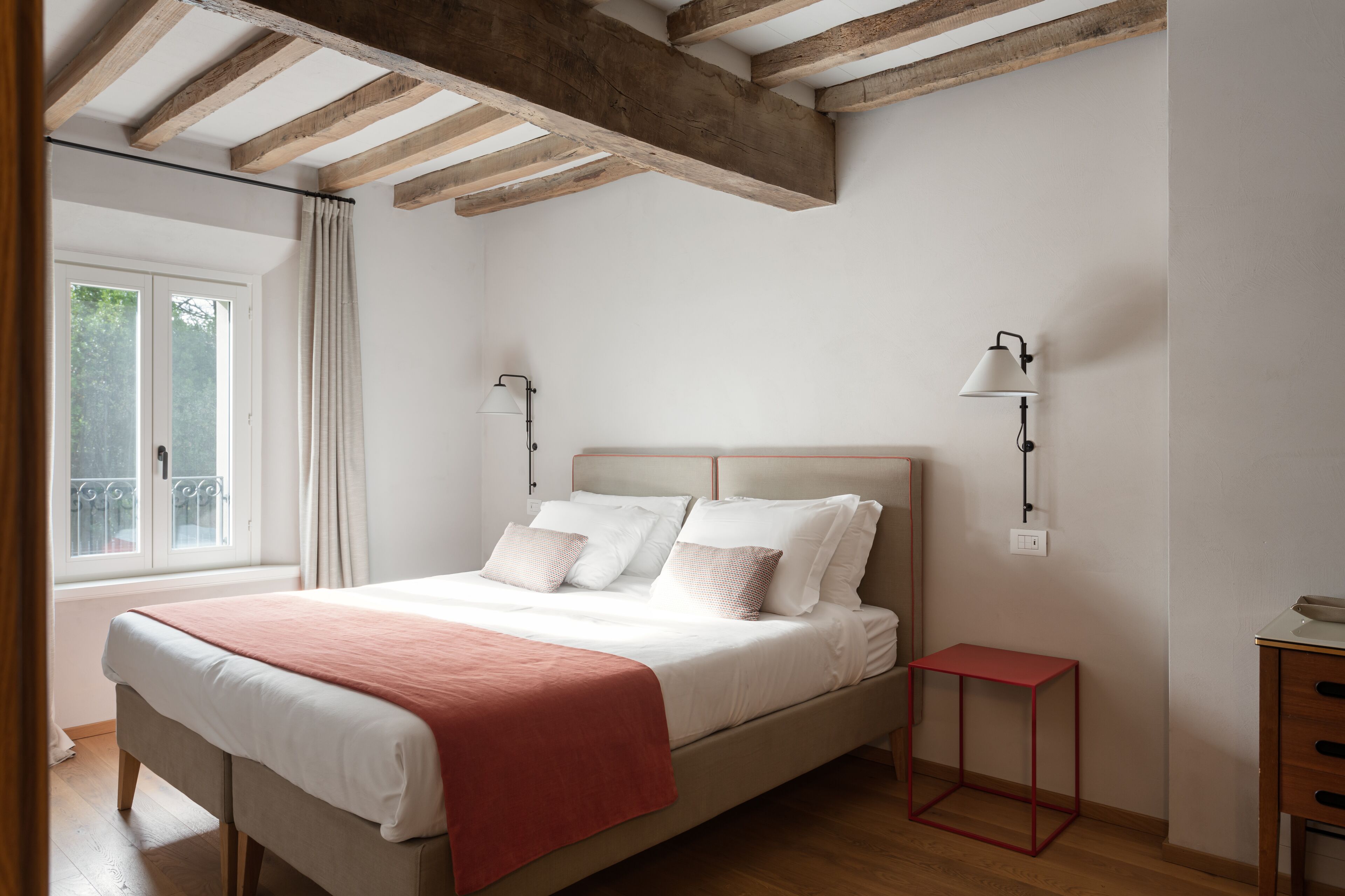 Un dormitorio con cama, lámparas de noche, una ventana y una mesita.