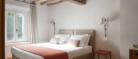Un dormitorio con cama, lámparas de noche, una ventana y una mesita.