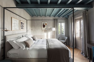 Quarto com cama de dossel, uma cadeira, uma escrivaninha e obras de arte nas paredes.