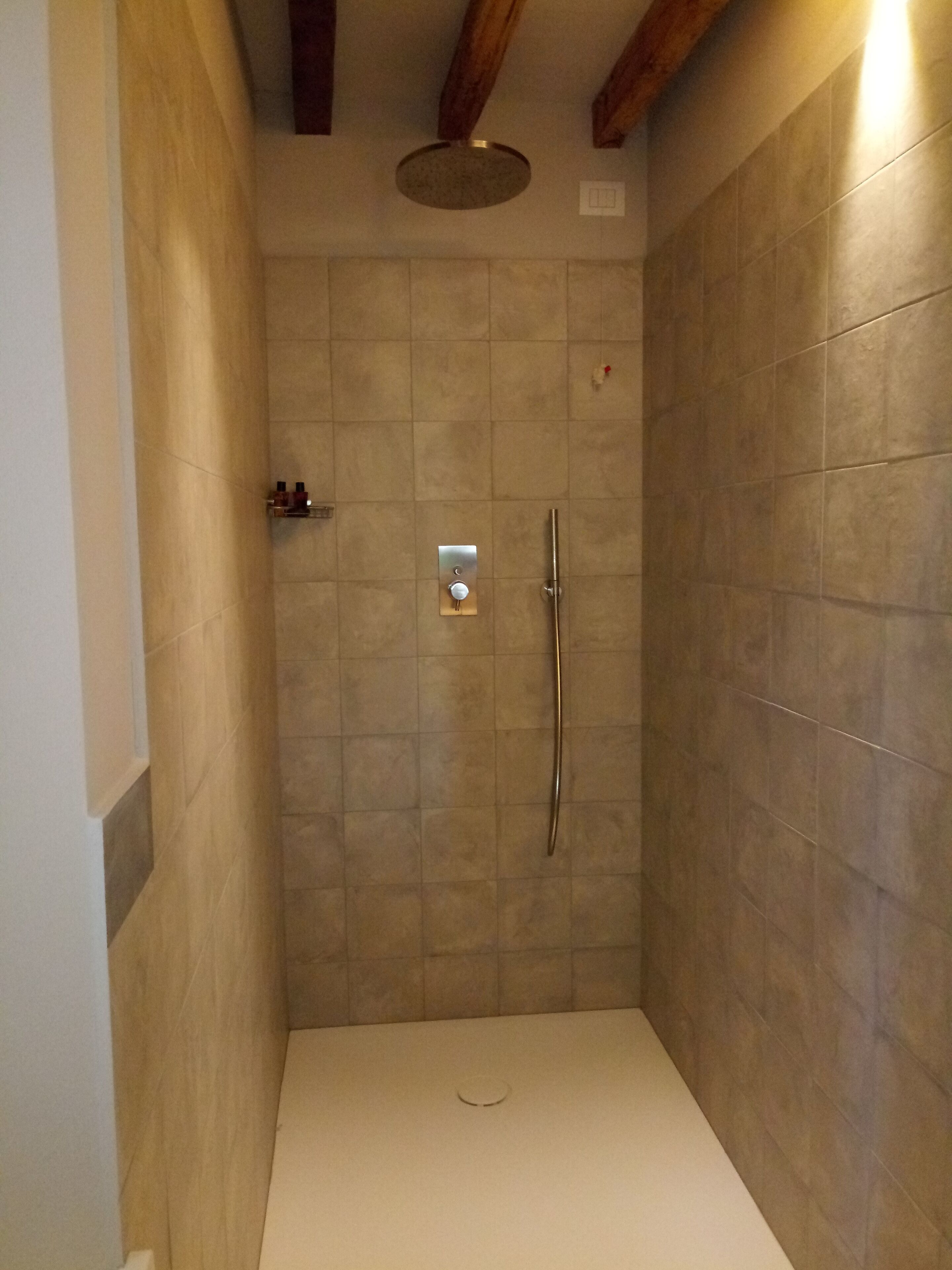 A small, enclosed shower area with a white floor, tiled walls, and a single showerhead.