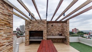 An outdoor patio with a wooden bench, a brick fireplace, and a view of the cityscape. - Nuestra Sra. de la Asunción Stylish Loft (Asunción)