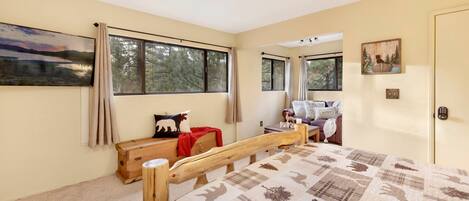 Un dormitorio con una cama de madera, un ventanal grande, un cuadro y una puerta con cerradura.