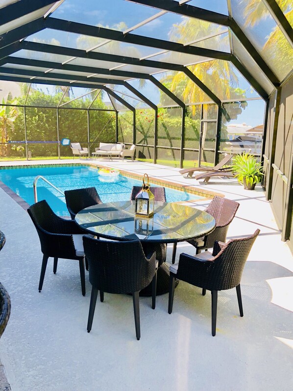 Un espacio al aire libre techado con piscina, asientos y una mesa.