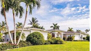 A two-story house with a well-maintained lawn and palm trees.