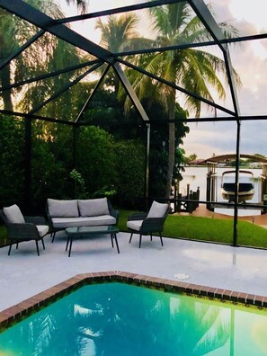 Un área de piscina al aire libre con una zona de estar cubierta, rodeada de abundante vegetación y palmeras.