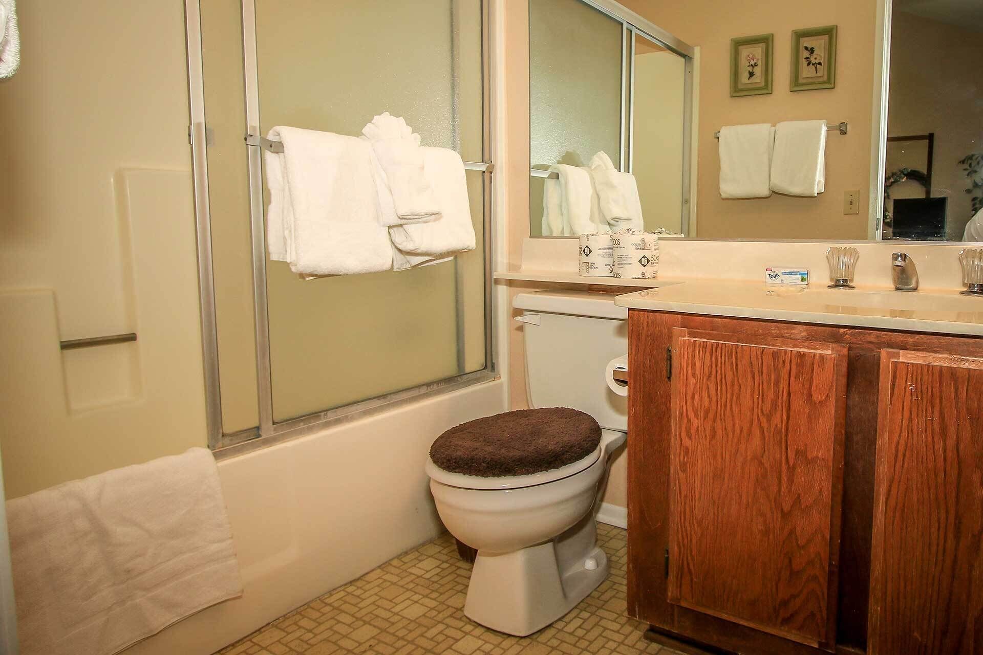 A bathroom with a toilet, a wooden cabinet, a sink, and a shower area.