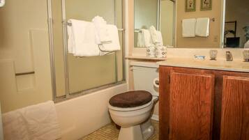 A bathroom with a toilet, a wooden cabinet, a sink, and a shower area.