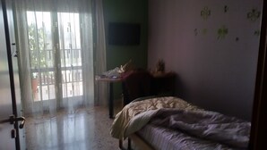 A bedroom with a bed, a desk, and a chair. There is a window with curtains and a view of the outside. - At Casa Peppe Partenopeo (Napoli)