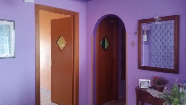 A hallway with purple walls, a wooden door, and a mirror on the right. - At Casa Peppe Partenopeo (Napoli)
