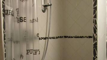 Une douche équipée d’un pommeau de douche à main et d’un rideau dont le texte est partiellement visible.