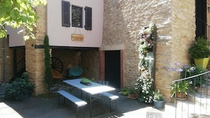 Un patio al aire libre con una mesa y bancos, rodeado de muros de piedra y plantas en macetas.