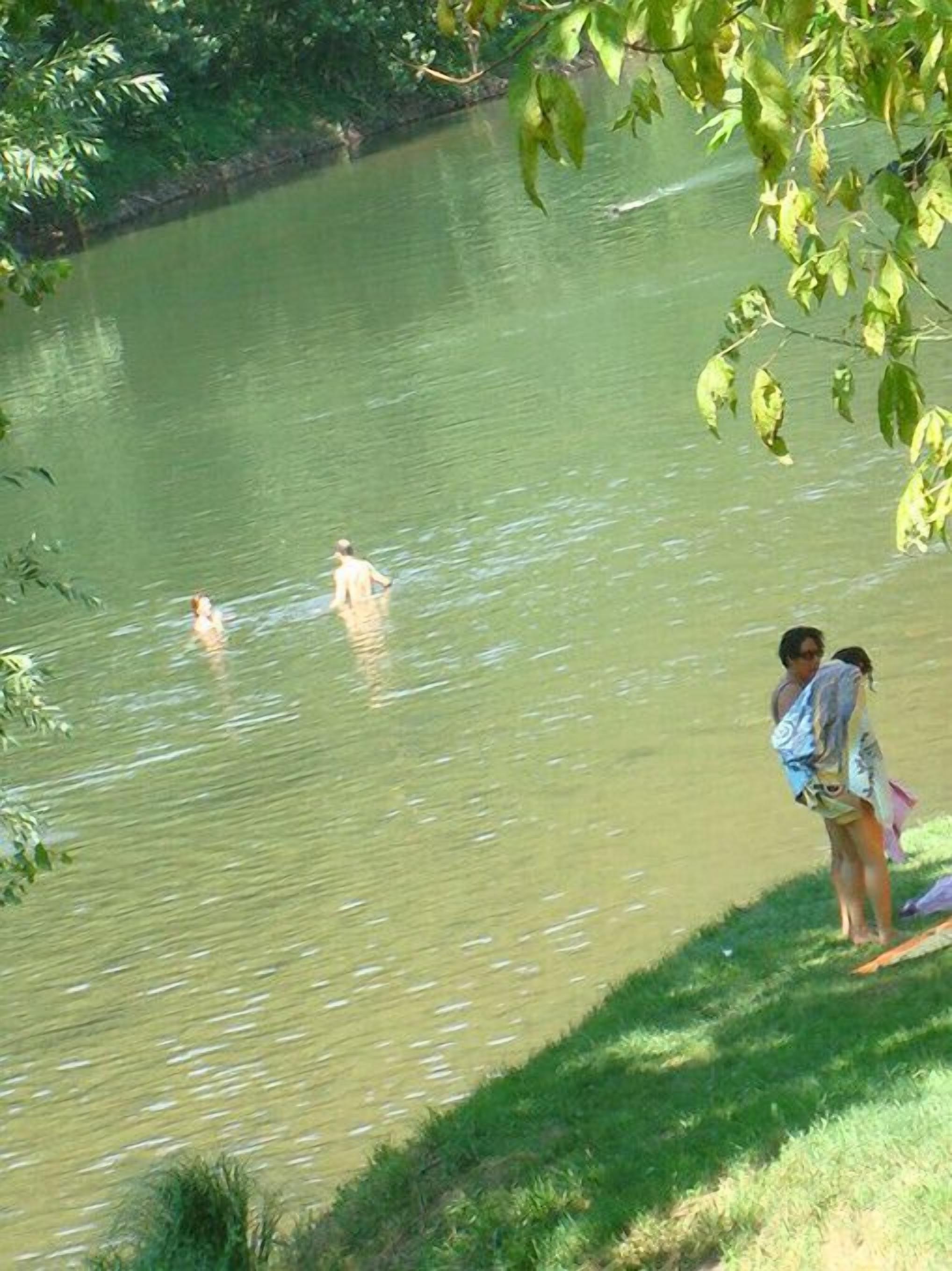 Un lago tranquilo con gente nadando y de pie en la orilla.
