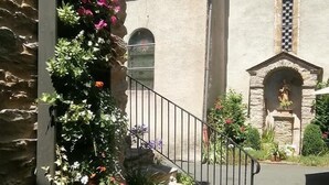 Un edificio de piedra con tejado de tejas, una estatua en un nicho arqueado y una escalera de metal que lleva a una puerta.