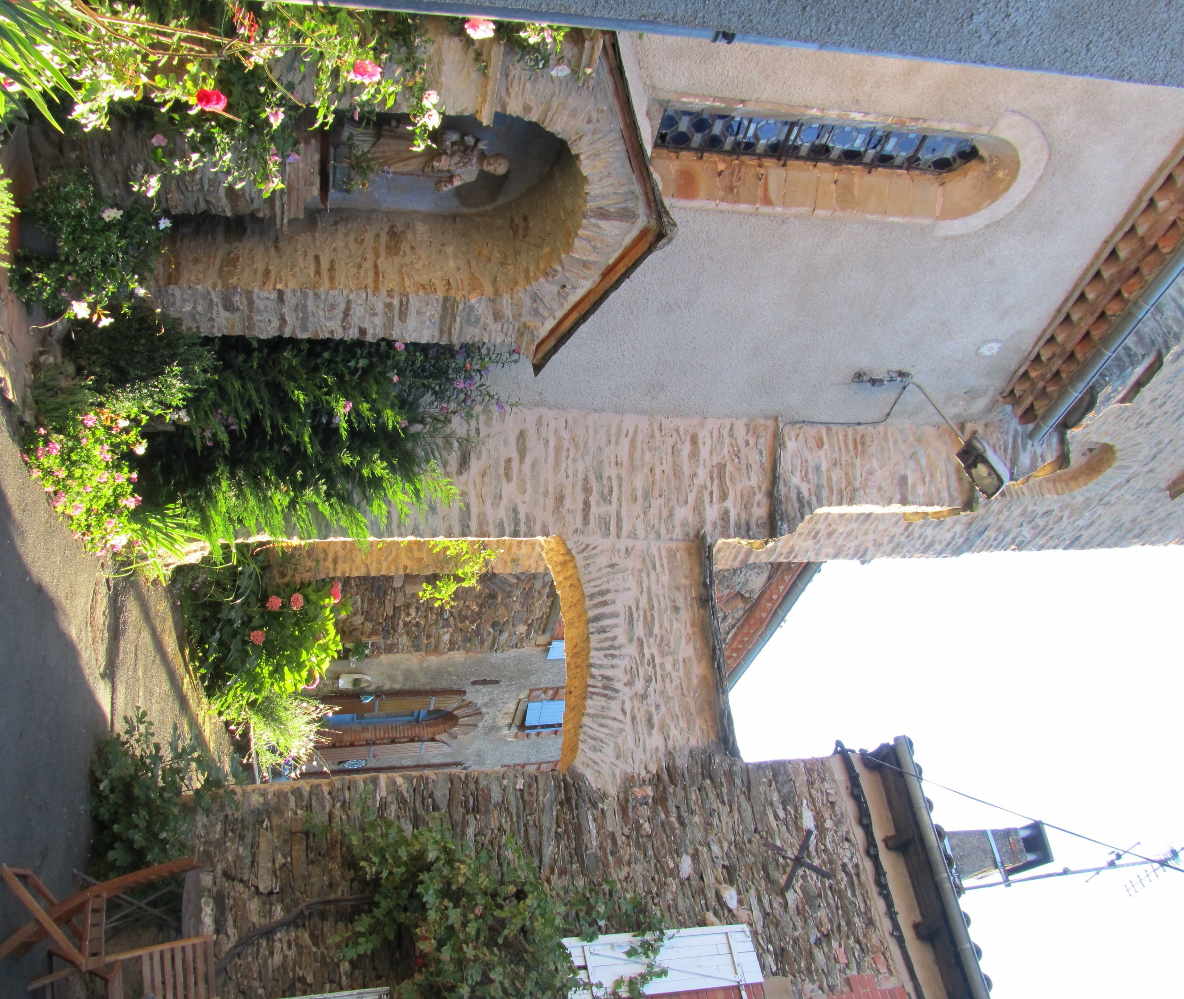 Ein Innenhof mit Steinmauern, einer Holzbank und einem kleinen Gartenbereich mit Blumen und Pflanzen.