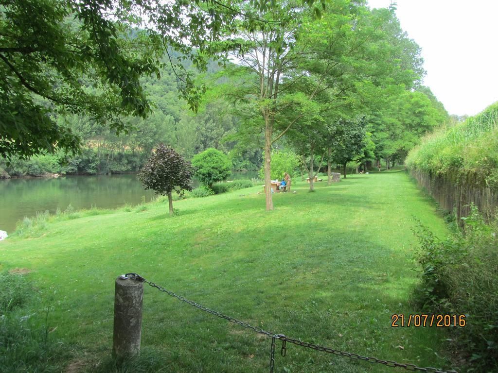A grassy area with a pond, trees, and a wooden post with a chain.