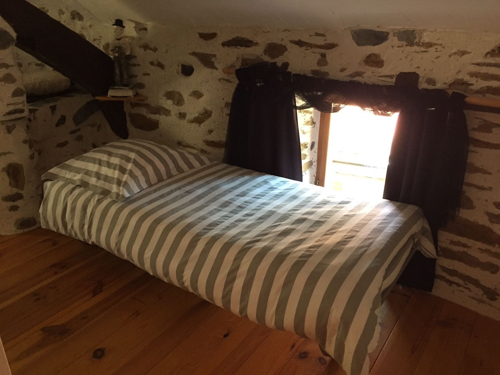 A small, cozy room with a single bed, a wooden floor, and a stone wall.