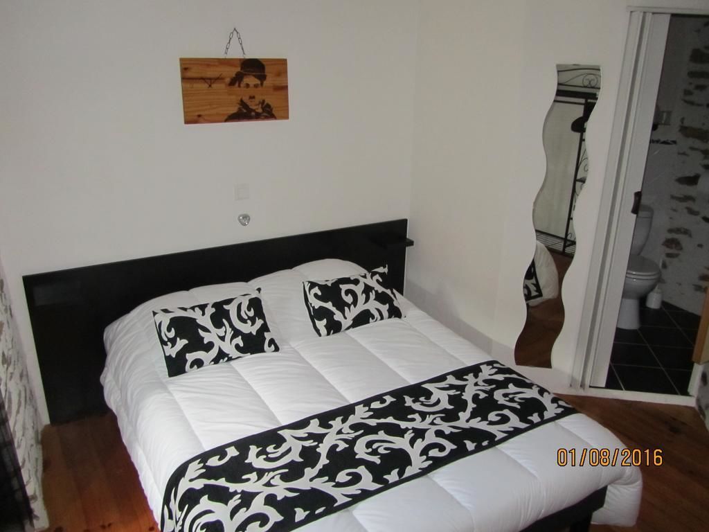 Une chambre à coucher avec un lit, une tête de lit en bois, une couvre-lit à motifs noir et blanc, un petit tableau en bois accroché au mur et une porte donnant sur une salle de bain.