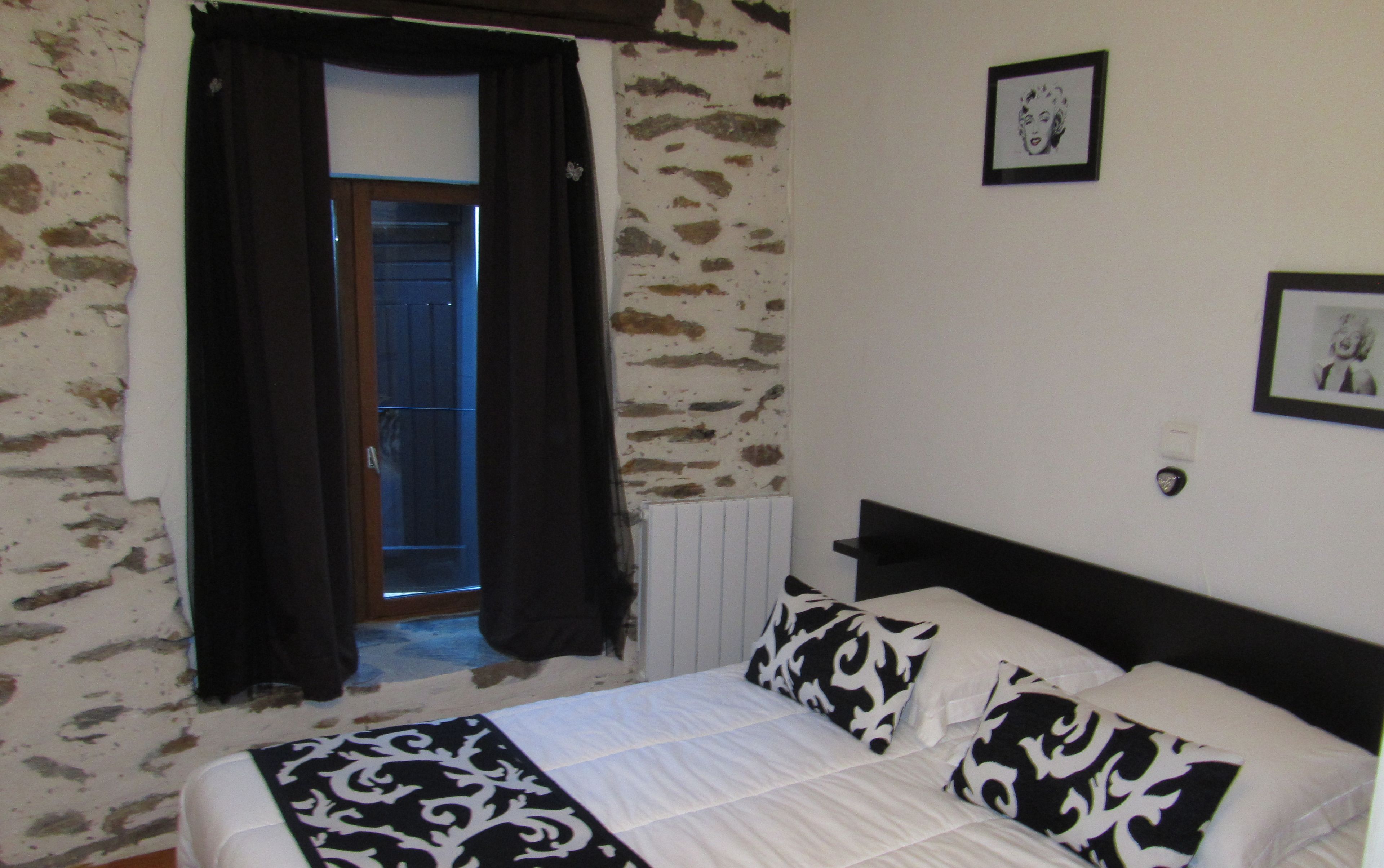 A bedroom with a bed, black and white patterned pillows, a window with curtains, and a radiator.