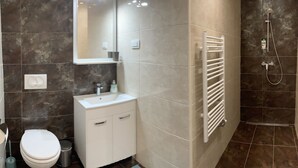 A bathroom with a toilet, sink, mirror, shower, and tiled walls.