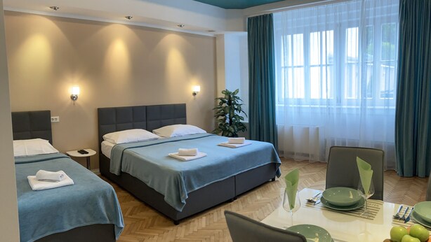 A hotel room with two beds, a dining table with plates and cutlery, and a large window with curtains.