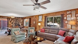 A cozy living room with a stone fireplace, wooden walls, and a large window offering a view of the outdoors. - Popko's Place #1426 (Big Bear Lake)