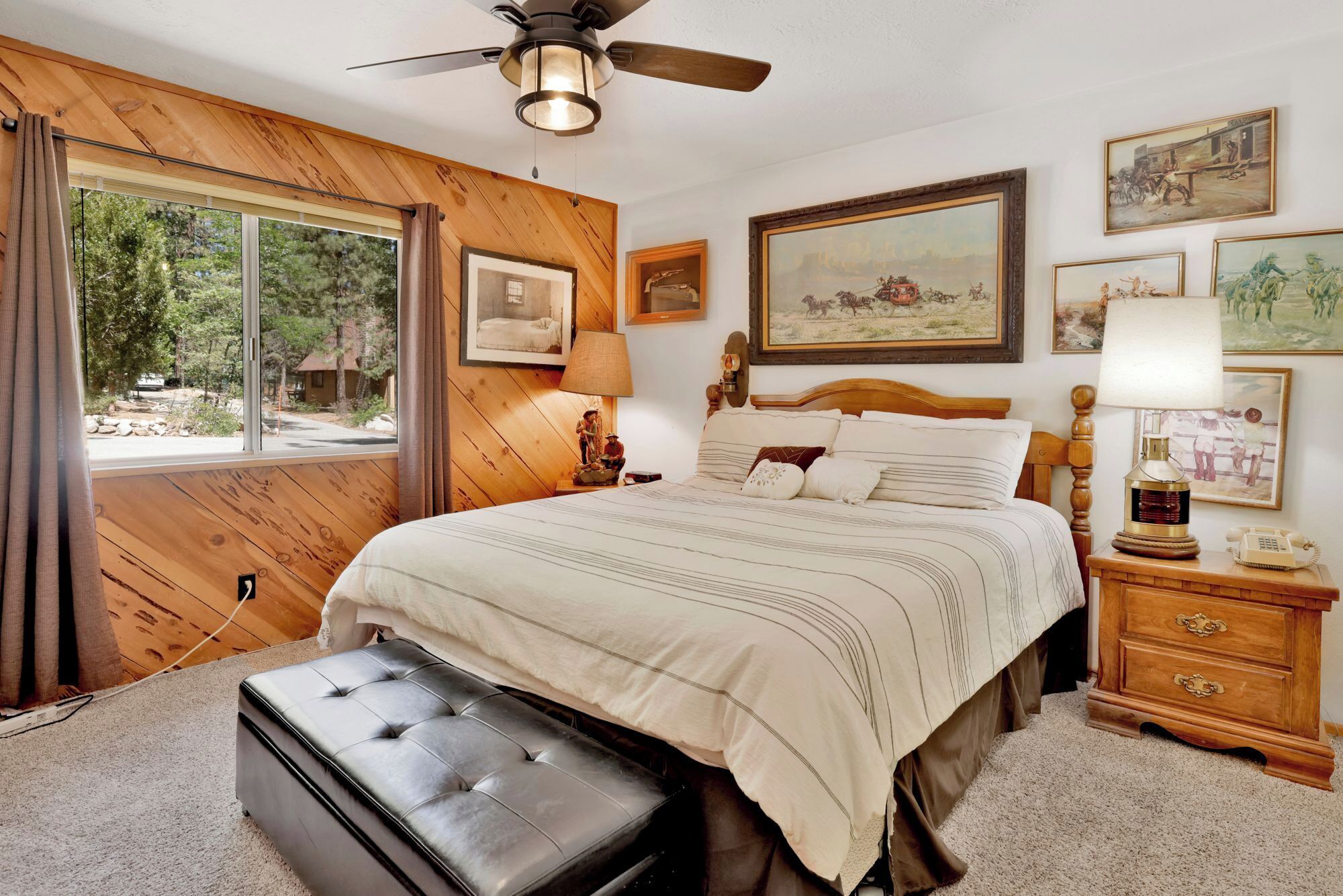 Ein Schlafzimmer mit einem großen Bett, Holzwandverkleidung, einem Deckenventilator und Kunstwerken an den Wänden.