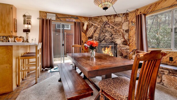 A cozy cabin interior with a stone wall fireplace, wooden dining table, and a bench. - Popko's Place #1426 (Big Bear Lake)